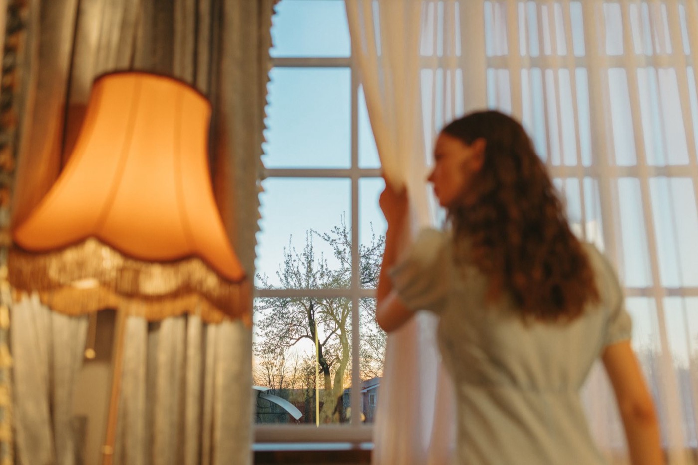A sheer curtain drawn back from a sash window, with a heavier drape panel hanging beside it.