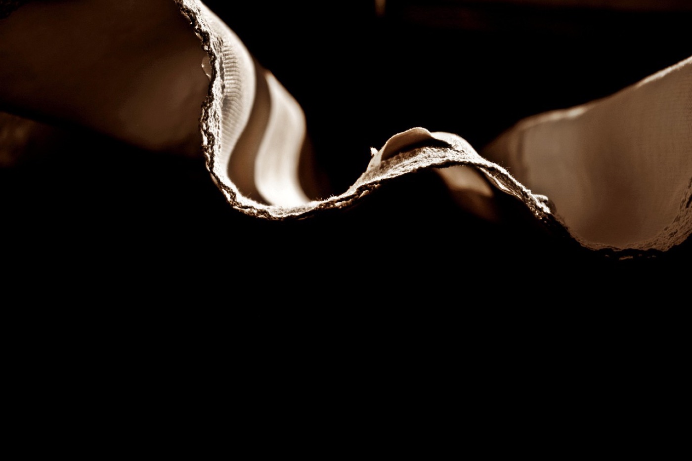 A backlit close-up of layered cream fabric, the edge of the face cloth lifted away from the layer behind it so the gap between the two is visible.