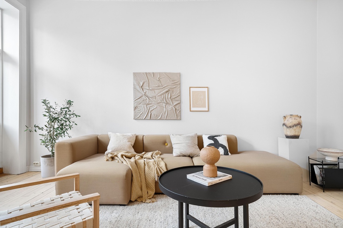 A sofa with three square cushions and a knitted throw draped over one arm, in a room with a pale rug and a round coffee table.