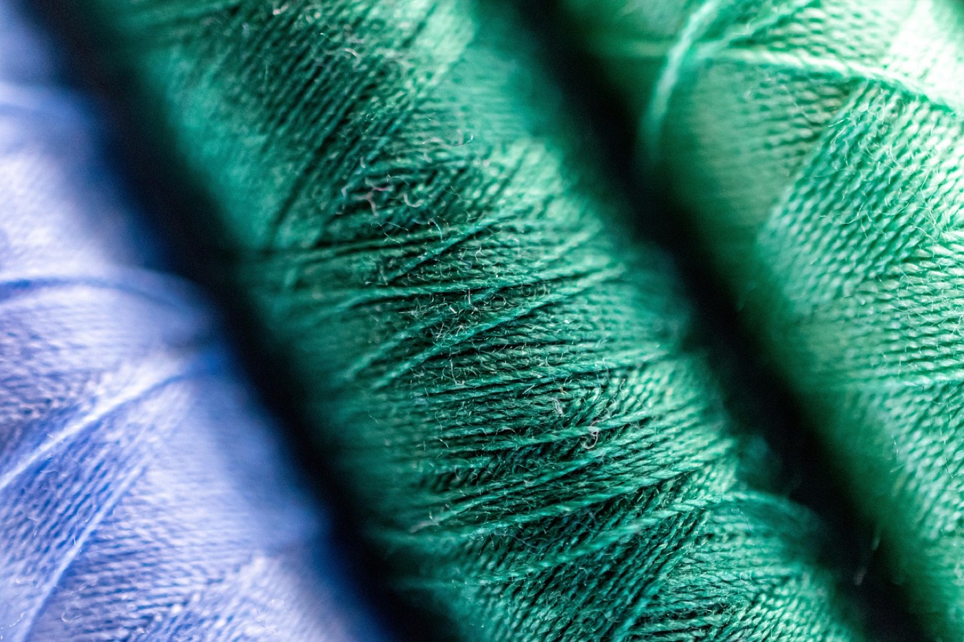 Two rolled rugs side by side in green wool and in pale synthetic fibre, showing how the surface fibres differ in texture and sheen.